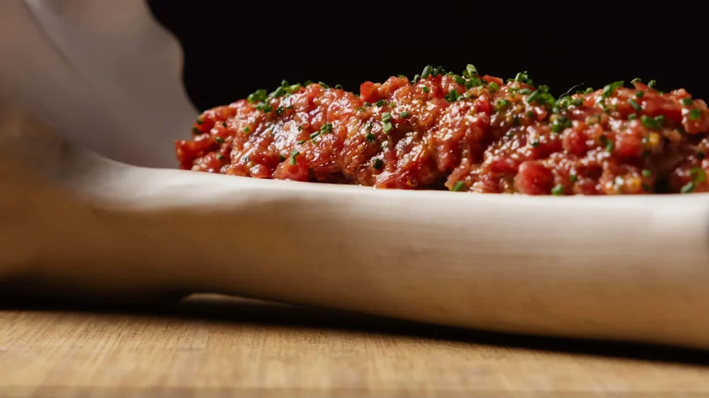 Steak tartar de buey con yema confitada al centro, servido en Carnal Steak House Barcelona, listo para mezclar en mesa